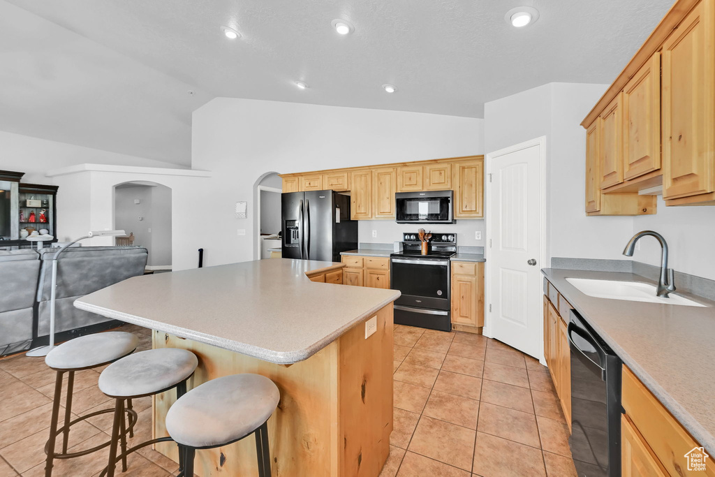 Kitchen with black appliances, arched walkways, a center island, a breakfast bar area, and light brown cabinetry