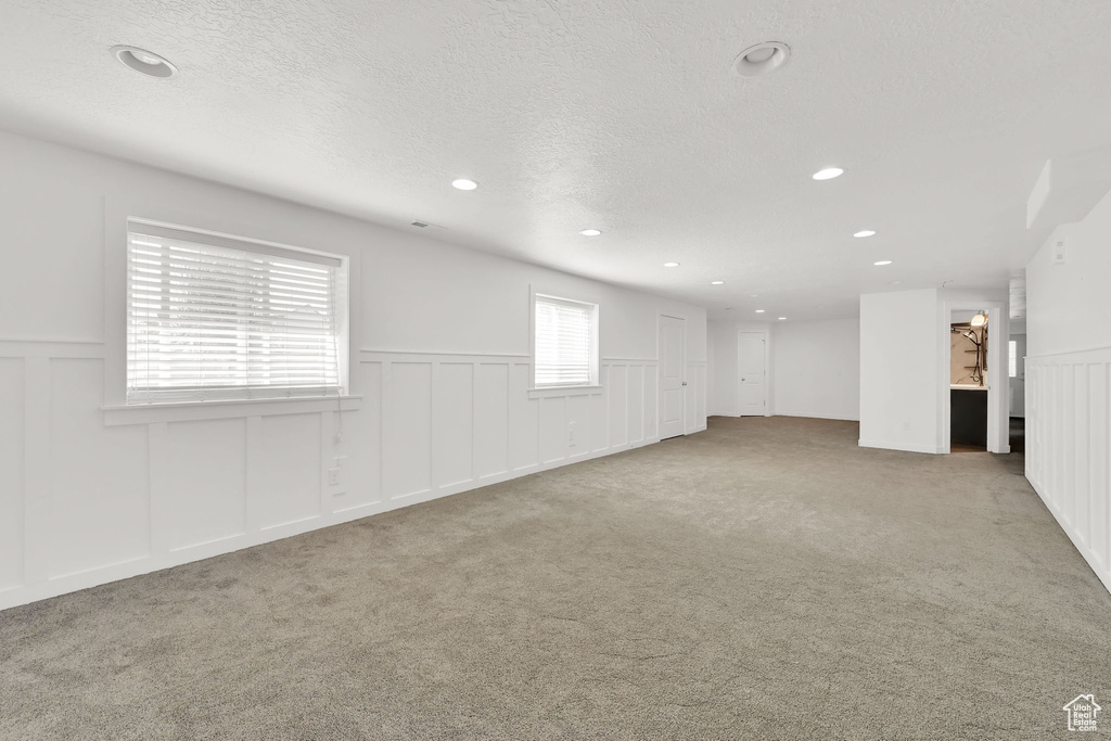 Unfurnished room featuring a decorative wall, a wainscoted wall, carpet, and a textured ceiling