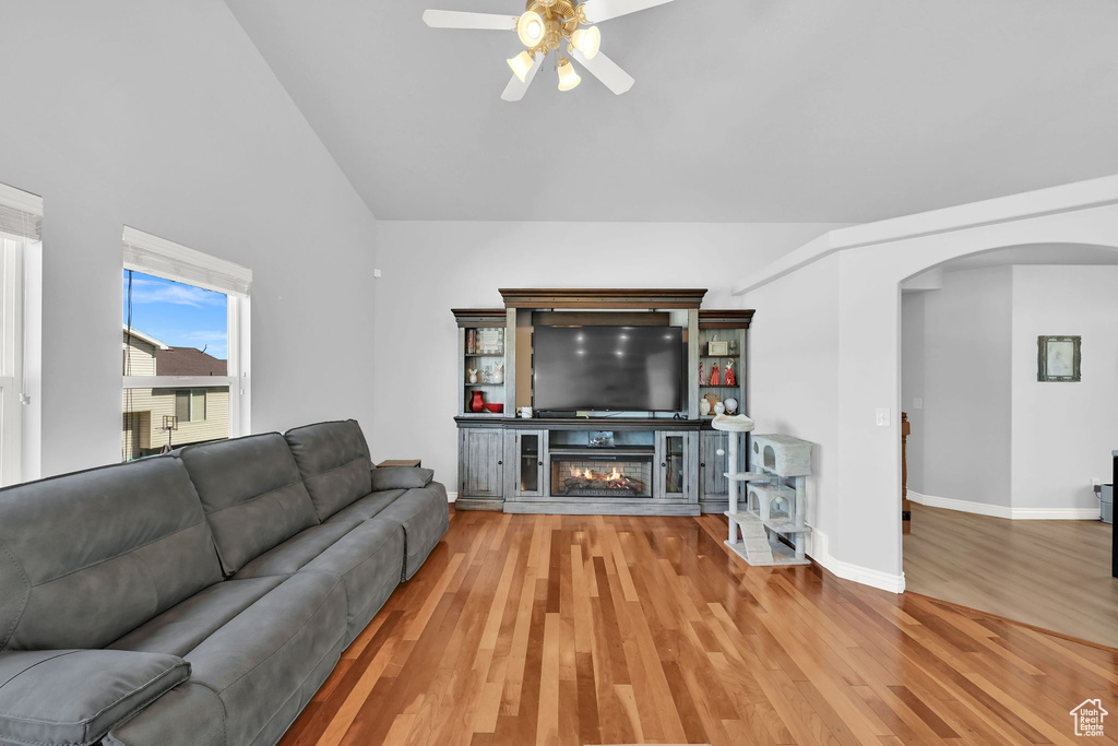 Living room featuring arched walkways, ceiling fan, wood finished floors, high vaulted ceiling, and a glass covered fireplace