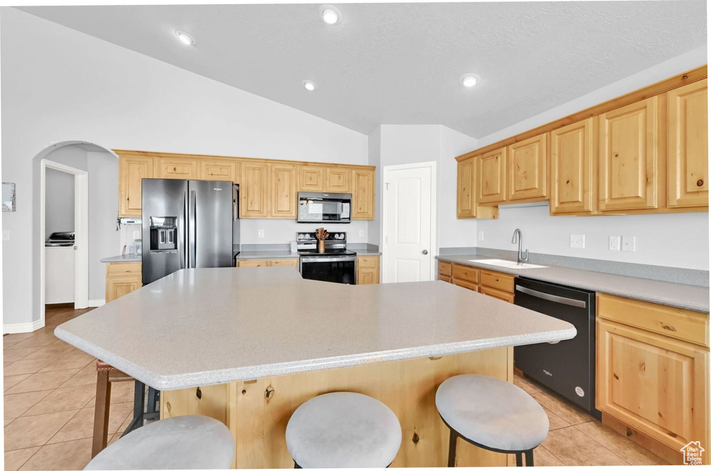 Kitchen with black appliances, light tile patterned floors, lofted ceiling, a breakfast bar area, and a kitchen island