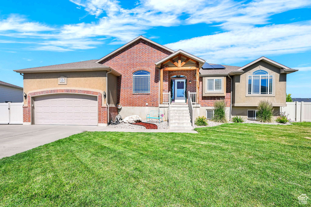 View of front of home featuring driveway, roof mounted solar panels, a garage, brick siding, and stucco siding