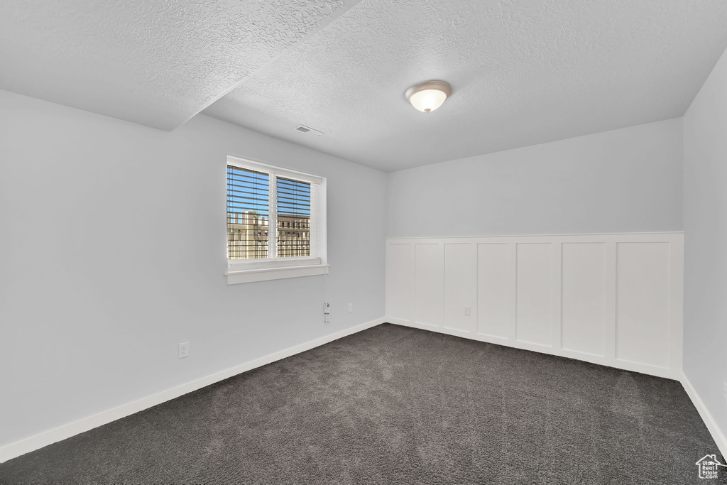 Spare room with a textured ceiling and dark carpet