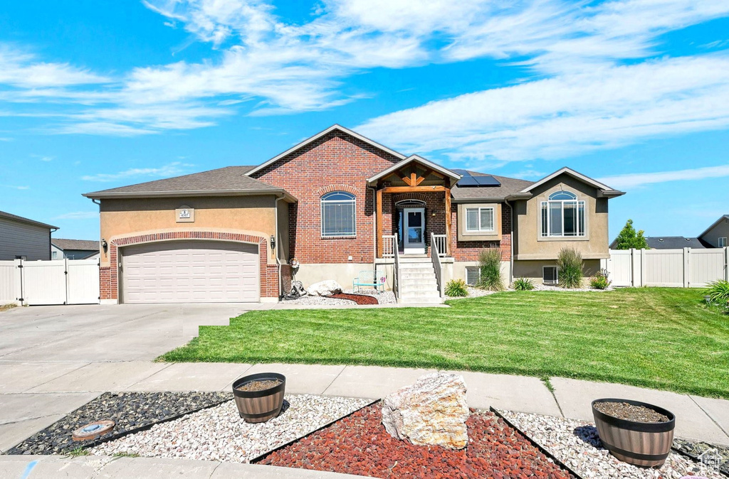 View of front facade featuring driveway, roof mounted solar panels, a garage, brick siding, and a gate