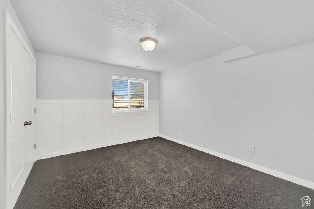 Spare room featuring a textured ceiling, a wainscoted wall, and dark carpet
