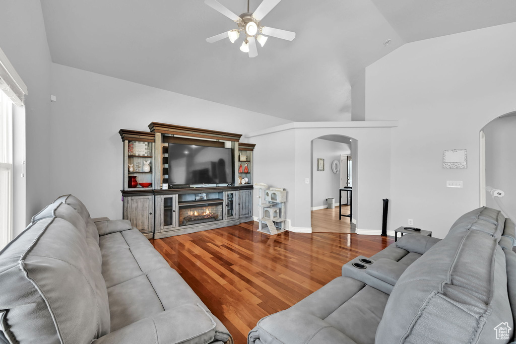 Living room featuring arched walkways, a ceiling fan, wood finished floors, vaulted ceiling, and a glass covered fireplace