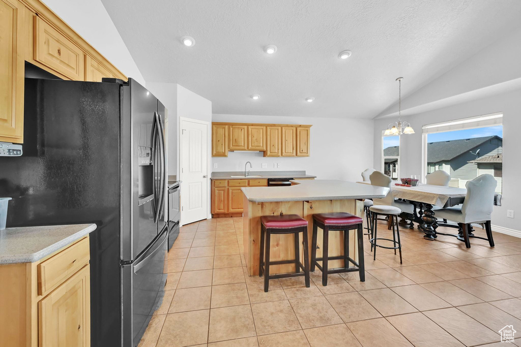 Kitchen featuring stainless steel fridge with ice dispenser, light countertops, range, vaulted ceiling, and a center island