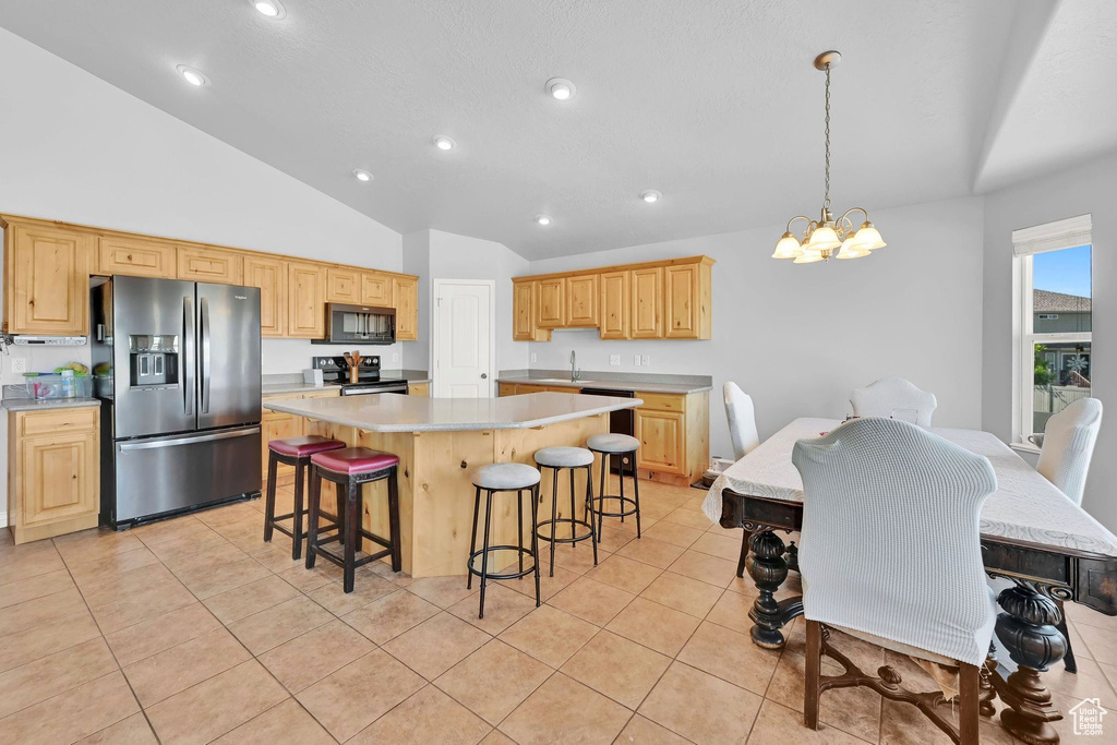 Kitchen with stainless steel appliances, light countertops, a center island, a chandelier, and vaulted ceiling