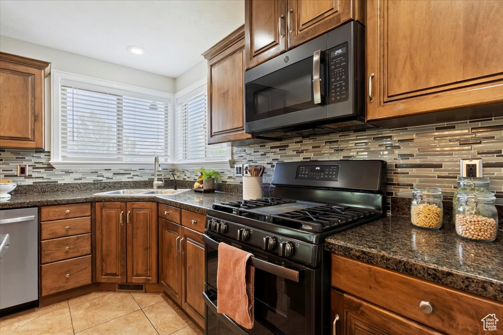 Kitchen featuring gas stove, stainless steel dishwasher, light tile patterned floors, backsplash, and brown cabinetry