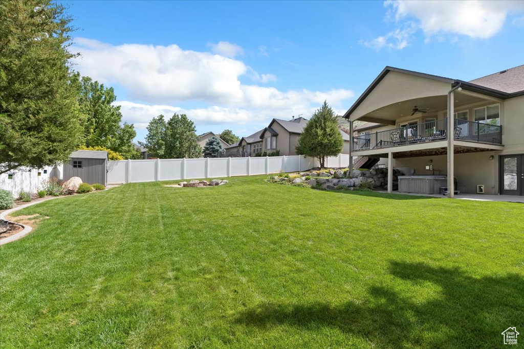 Fenced backyard with a hot tub, ceiling fan, and a storage shed