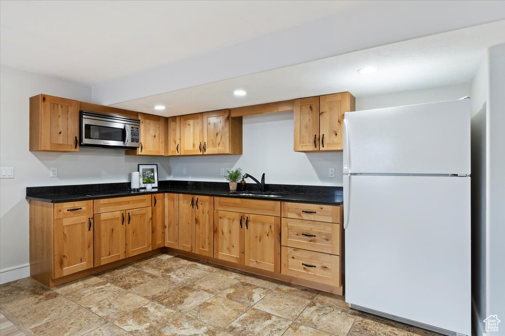 Kitchen with freestanding refrigerator, stainless steel microwave, light stone finish flooring, recessed lighting, and dark stone counters