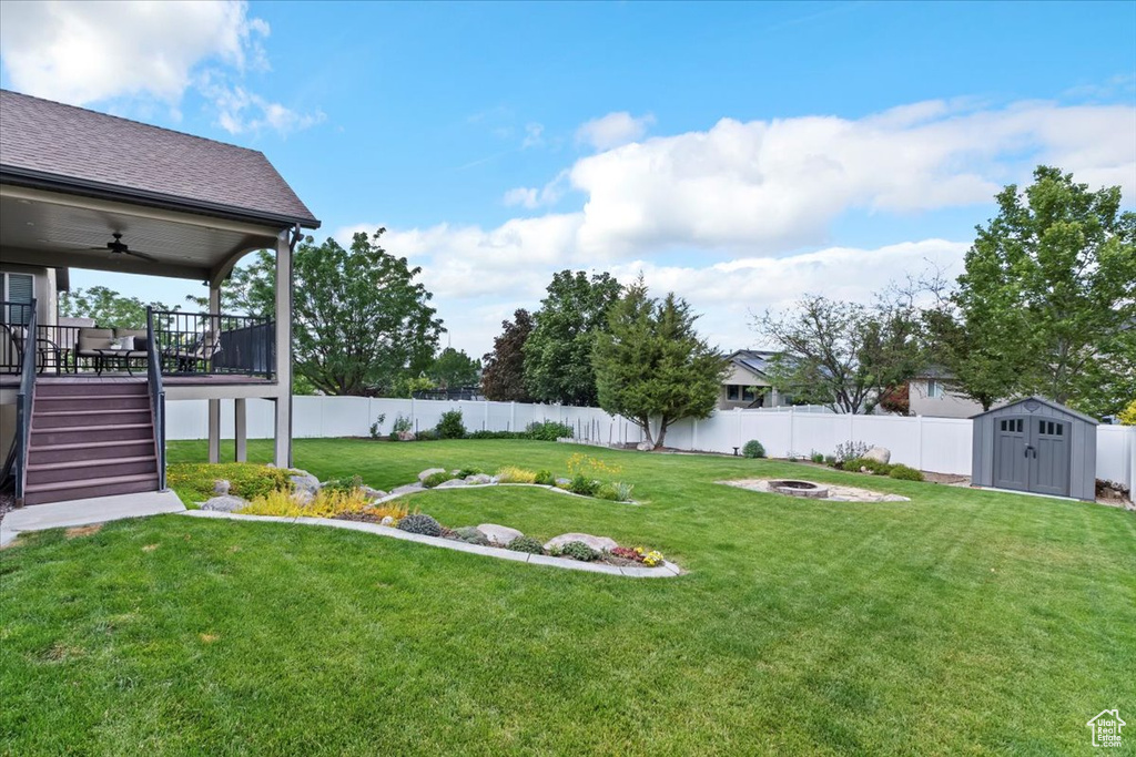 Fenced backyard featuring an outdoor fire pit, a storage shed, a ceiling fan, a deck, and stairway
