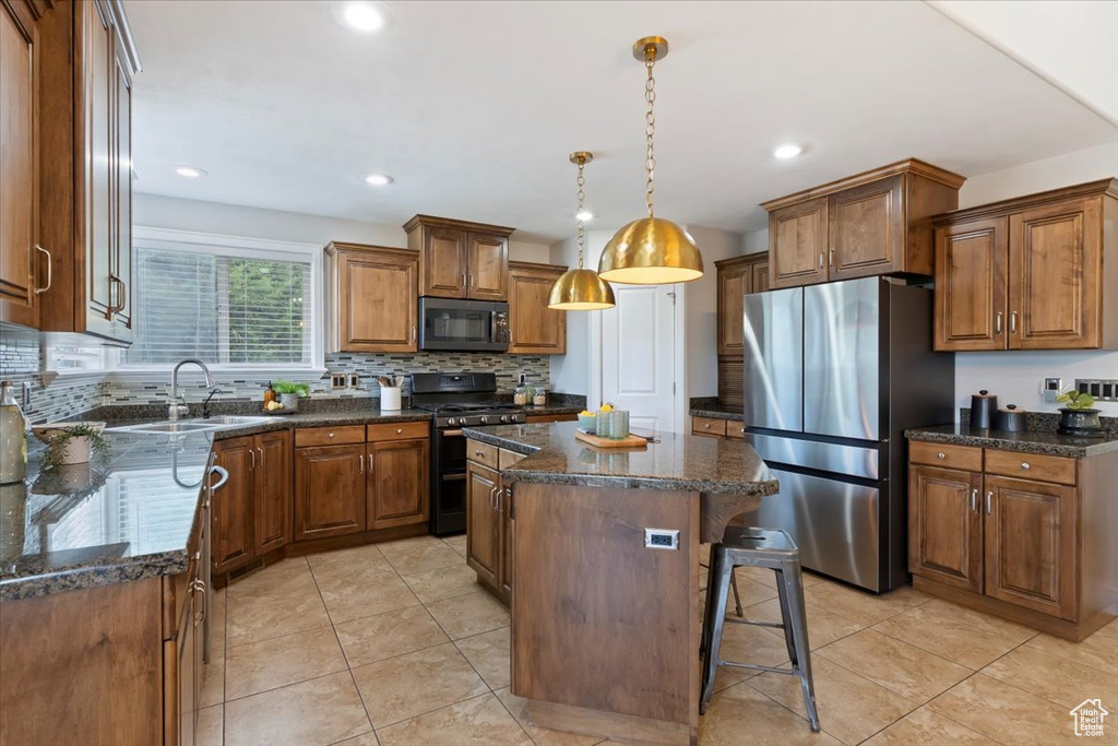 Kitchen featuring freestanding refrigerator, gas range oven, a center island, brown cabinets, and tasteful backsplash