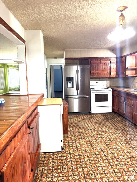 Kitchen featuring stainless steel refrigerator with ice dispenser, white electric range oven, and a textured ceiling