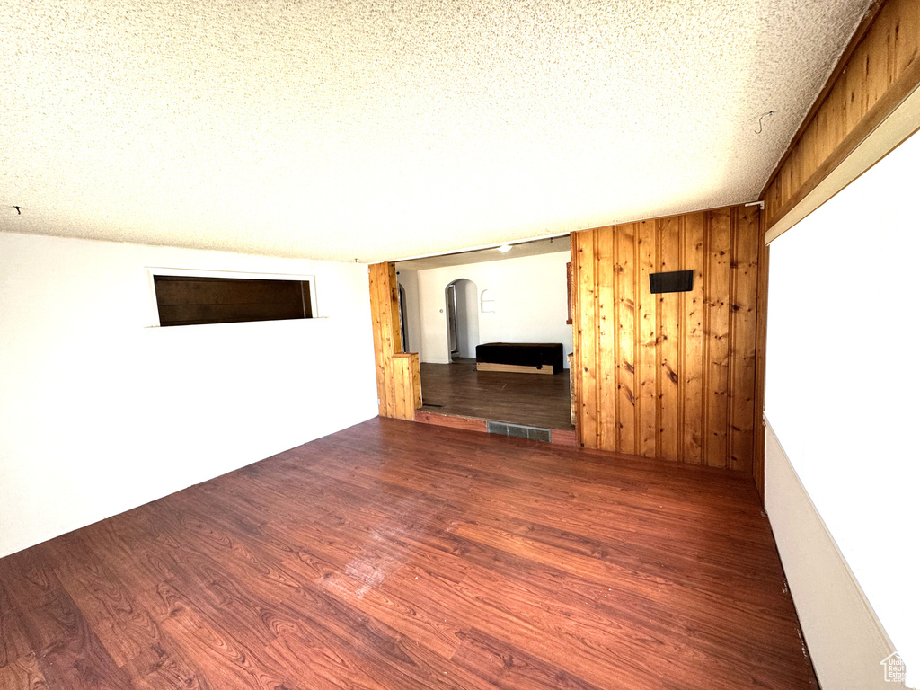 Empty room with arched walkways, wood finished floors, wooden walls, and a textured ceiling