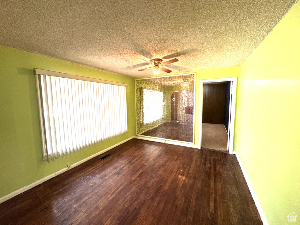 Empty room with wood finished floors, ceiling fan, and a textured ceiling