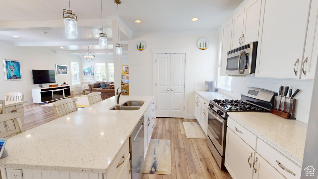 Kitchen with stainless steel appliances, light wood-type flooring, a center island with sink, white cabinetry, and recessed lighting