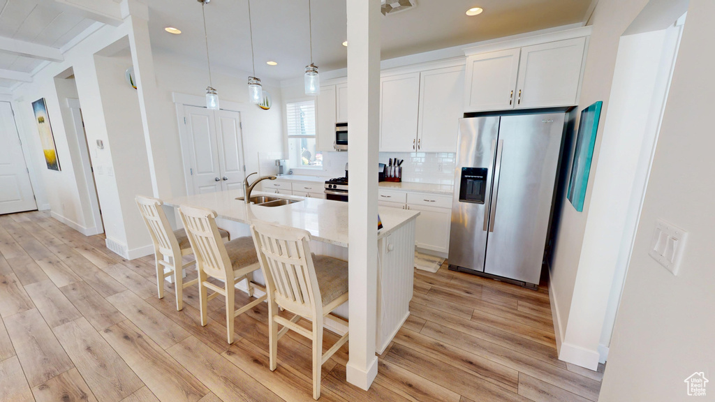 Kitchen with stainless steel fridge with ice dispenser, a center island with sink, recessed lighting, light wood-style floors, and light countertops