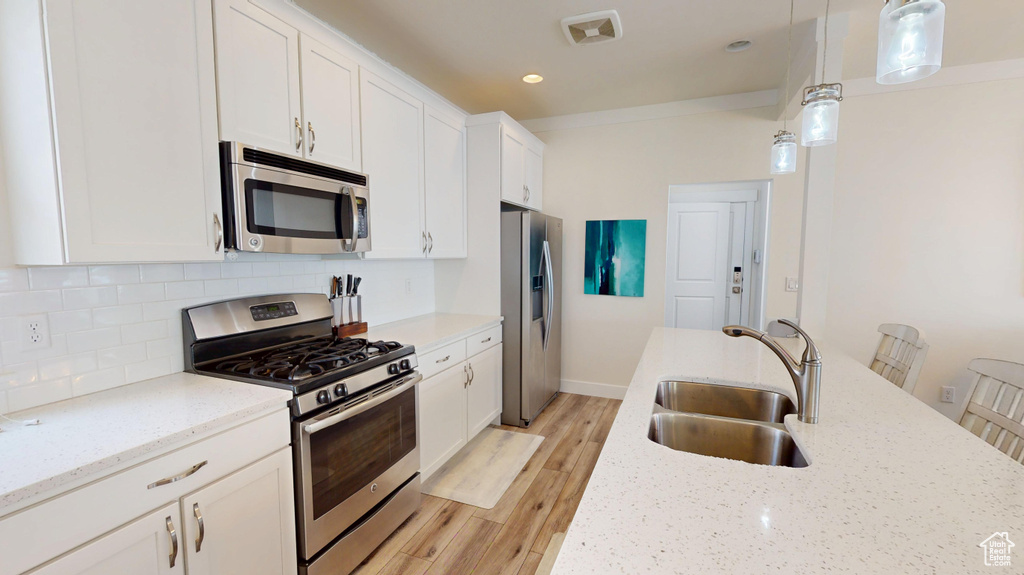 Kitchen with stainless steel appliances, tasteful backsplash, white cabinetry, light wood-type flooring, and pendant lighting