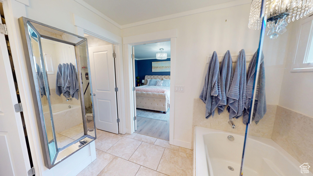 Ensuite bathroom with a bath, a chandelier, ornamental molding, and tile patterned floors