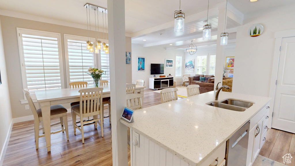 Kitchen featuring stainless steel dishwasher, light wood finished floors, beam ceiling, a center island with sink, and a chandelier