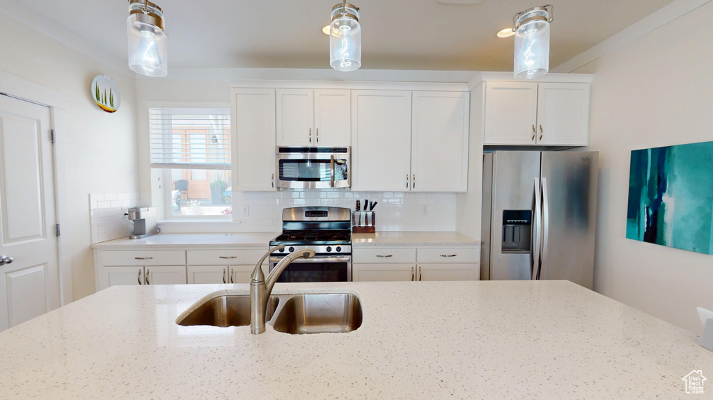 Kitchen with appliances with stainless steel finishes, decorative light fixtures, decorative backsplash, and light stone counters