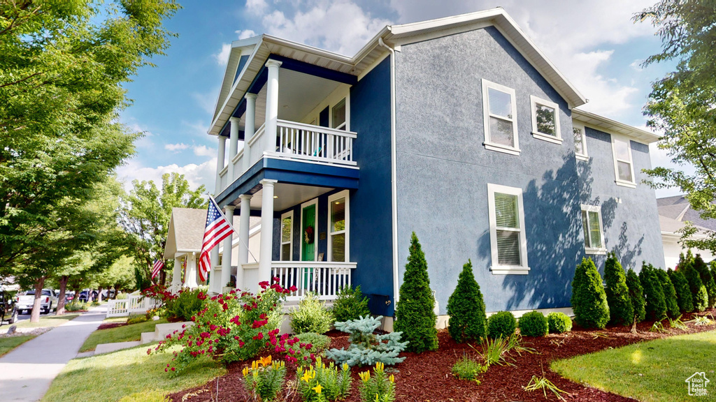 View of side of property featuring a balcony, stucco siding, and a porch