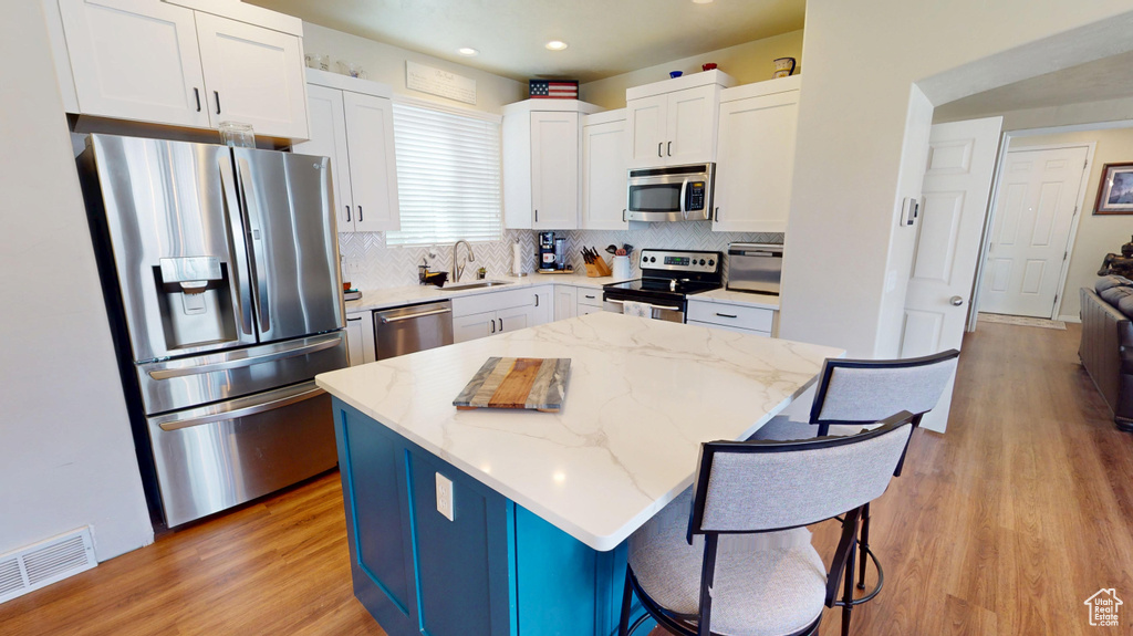 Kitchen with stainless steel appliances, a kitchen island, light wood-style flooring, light stone countertops, and white cabinets