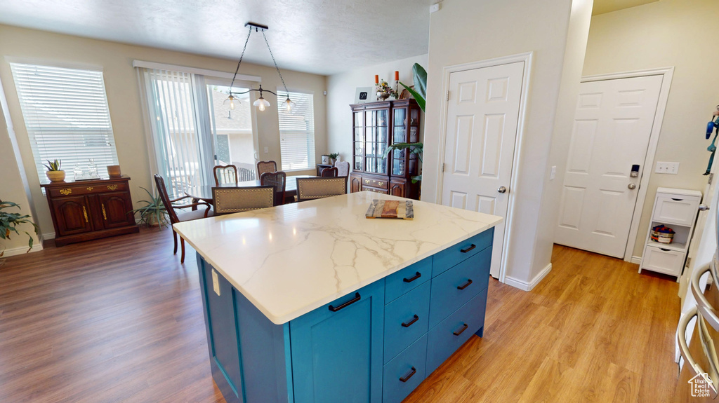Kitchen featuring blue cabinets, light wood-style floors, a center island, and pendant lighting
