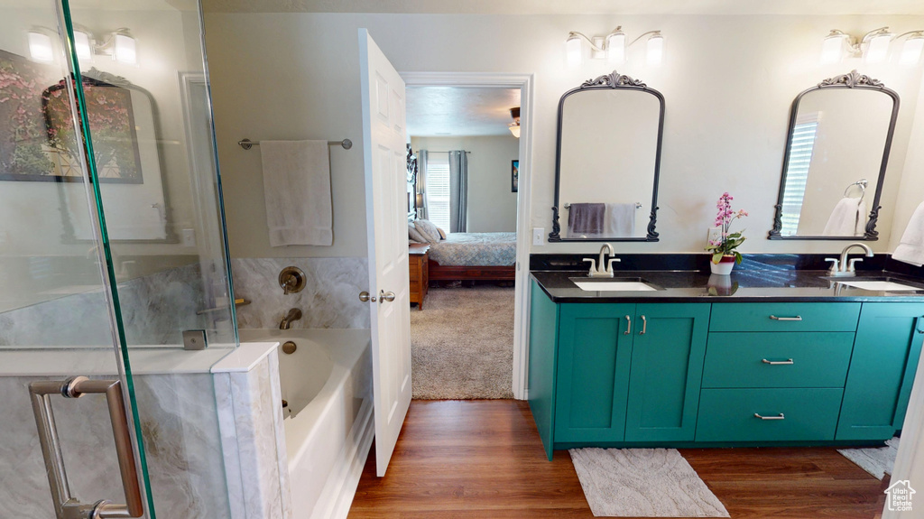 Ensuite bathroom featuring a garden tub, double vanity, wood finished floors, and a shower with door