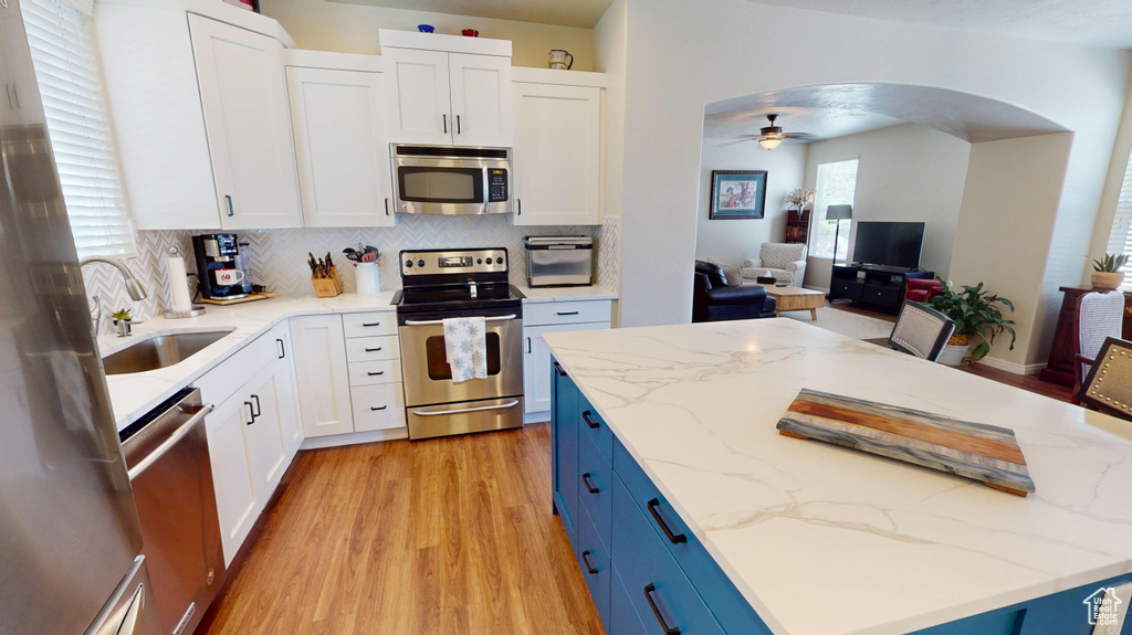 Kitchen featuring stainless steel appliances, blue cabinetry, ceiling fan, light wood-type flooring, and open floor plan