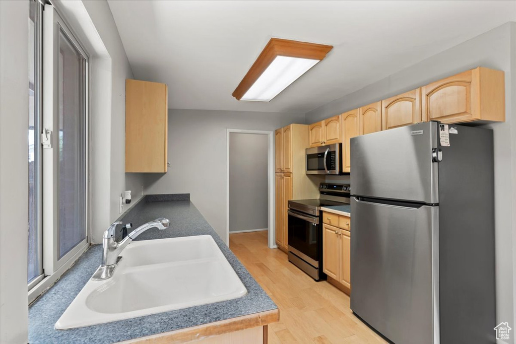 Kitchen with stainless steel appliances, light brown cabinetry, light wood-style flooring, and dark countertops