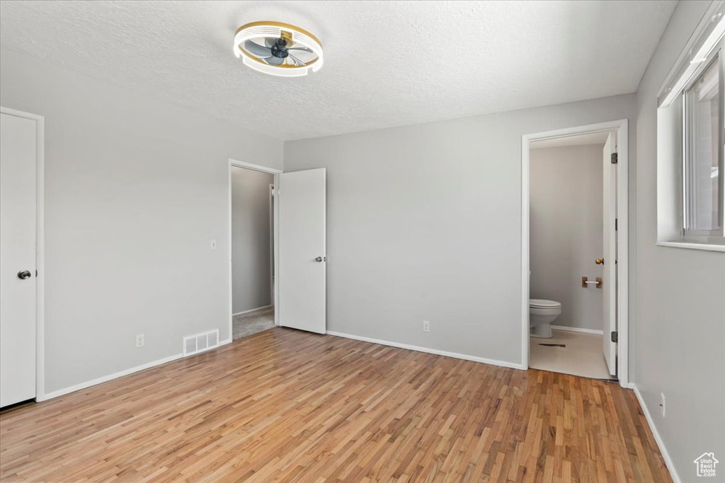 Unfurnished bedroom featuring light wood-style floors, ensuite bathroom, and a textured ceiling
