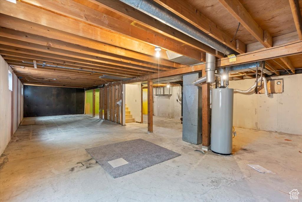 Unfinished below grade area with gas water heater, stairs, and heating unit