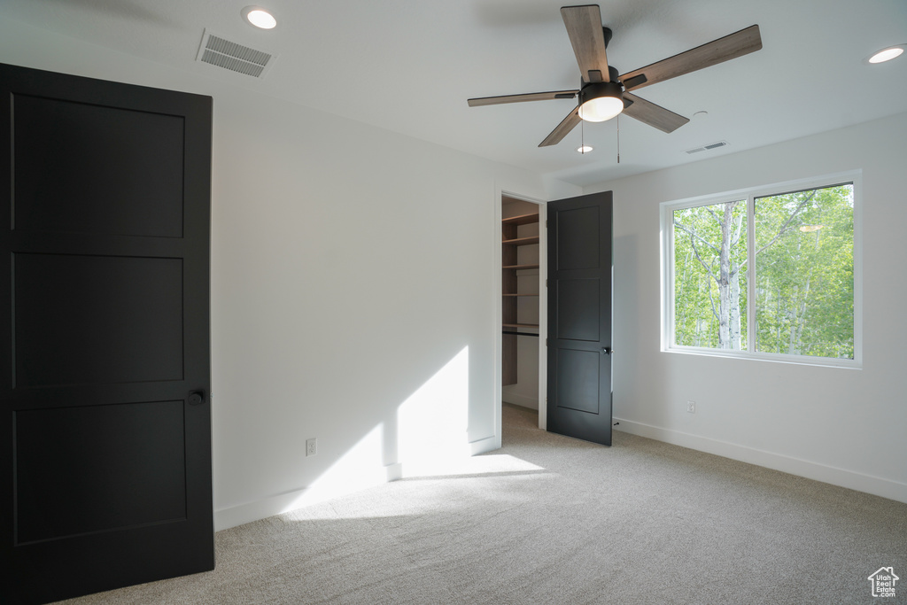 Unfurnished bedroom featuring light colored carpet, recessed lighting, a walk in closet, and a ceiling fan