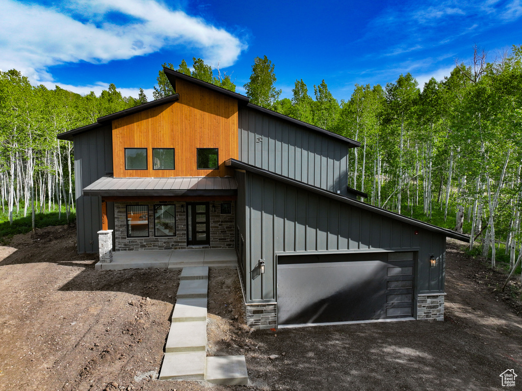 Contemporary home featuring a metal roof, stone siding, dirt driveway, a porch, and a standing seam roof