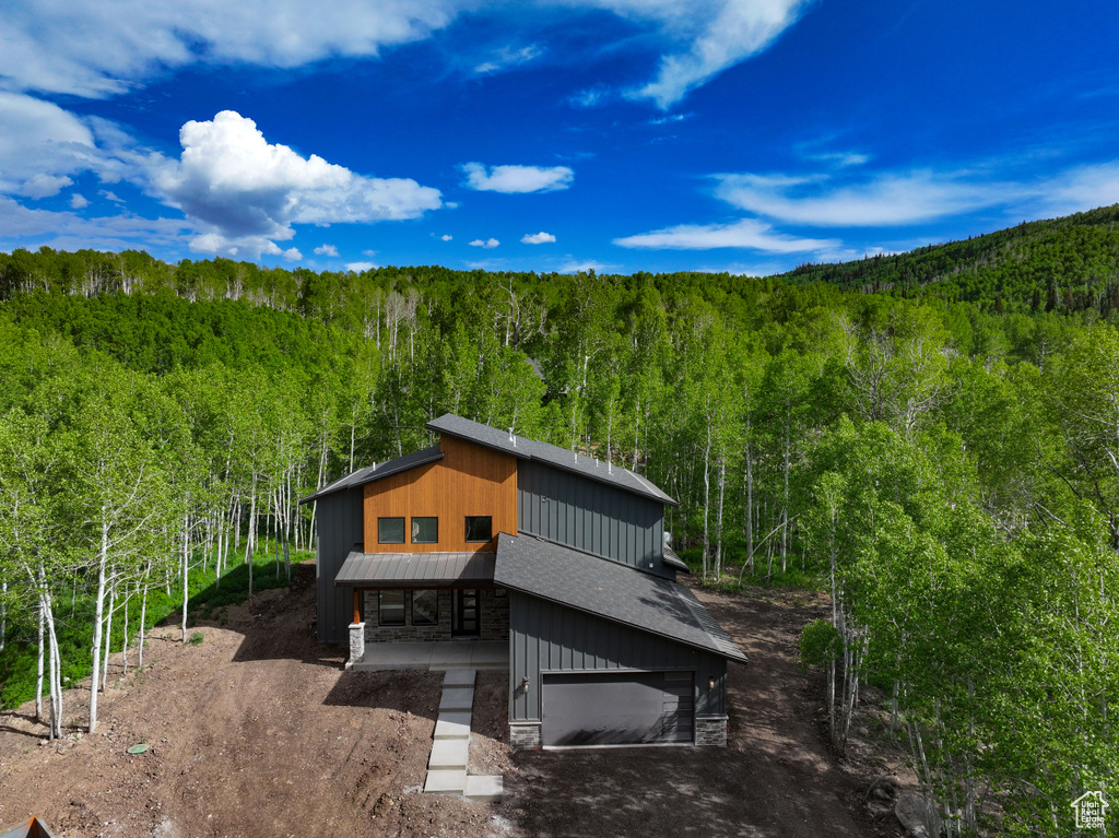 Exterior space with a forest view, stone siding, driveway, a garage, and a metal roof