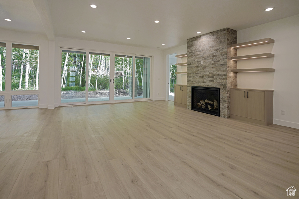 Unfurnished living room with light wood-type flooring, healthy amount of natural light, recessed lighting, and a large fireplace