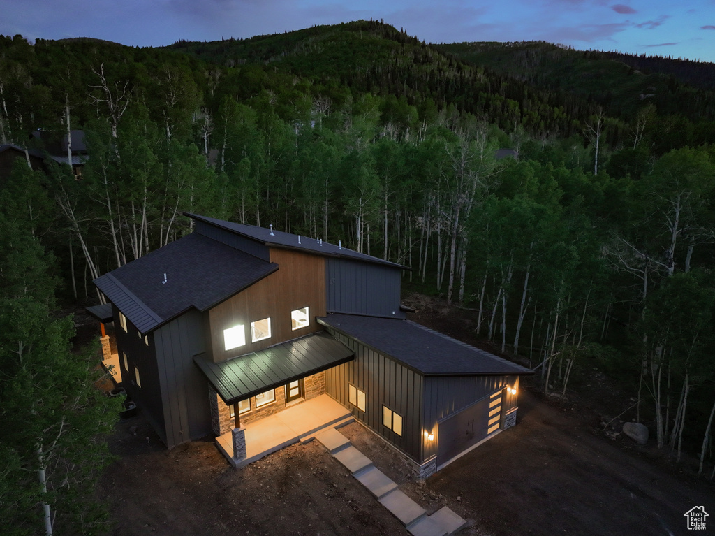 Back of house with a wooded view, a standing seam roof, a metal roof, roof with shingles, and driveway