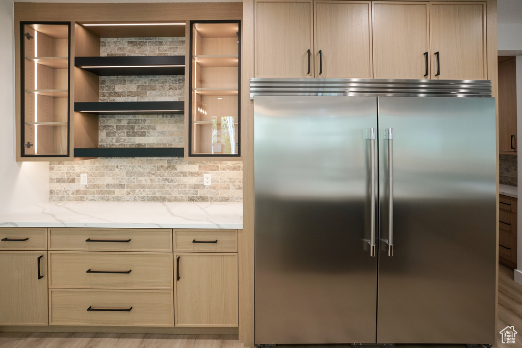 Kitchen featuring built in refrigerator, light stone countertops, and light brown cabinetry