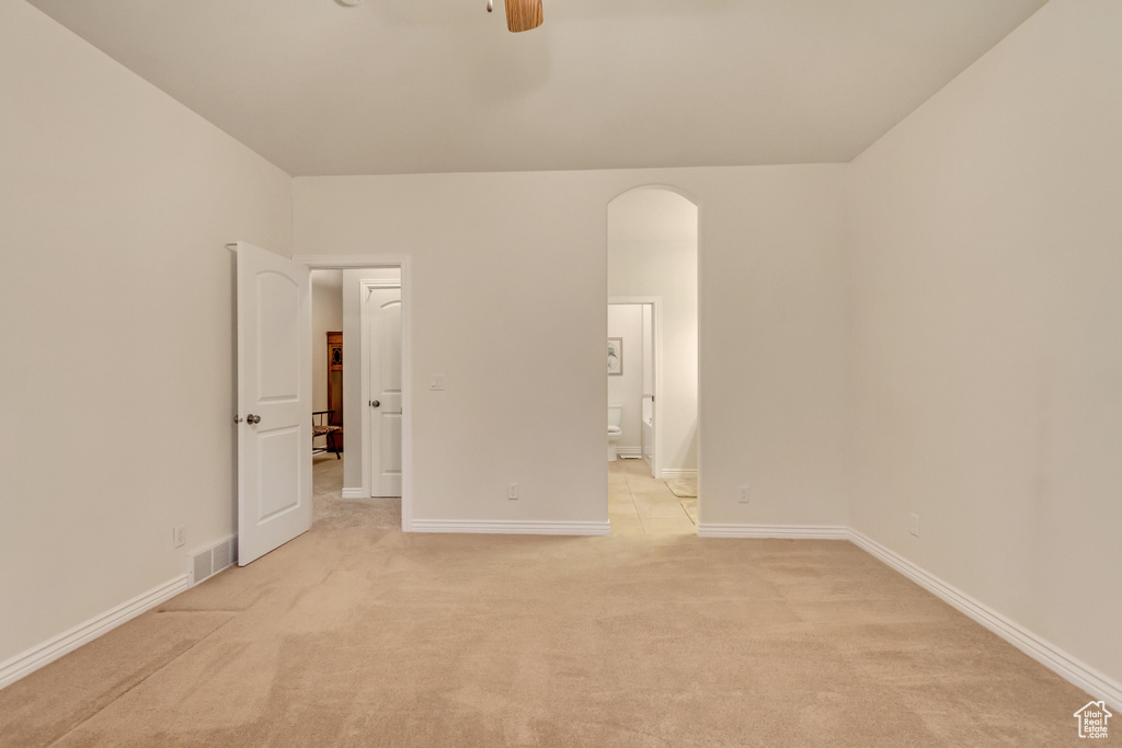 Unfurnished bedroom with light colored carpet, ensuite bathroom, and arched walkways