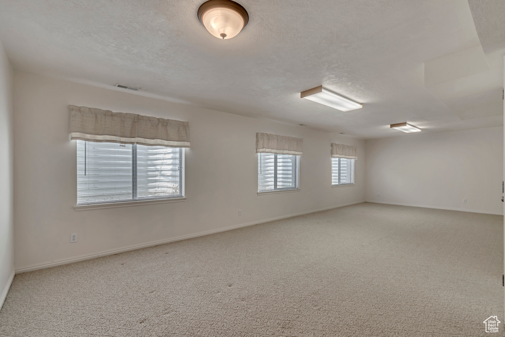 Carpeted spare room featuring a textured ceiling and baseboards