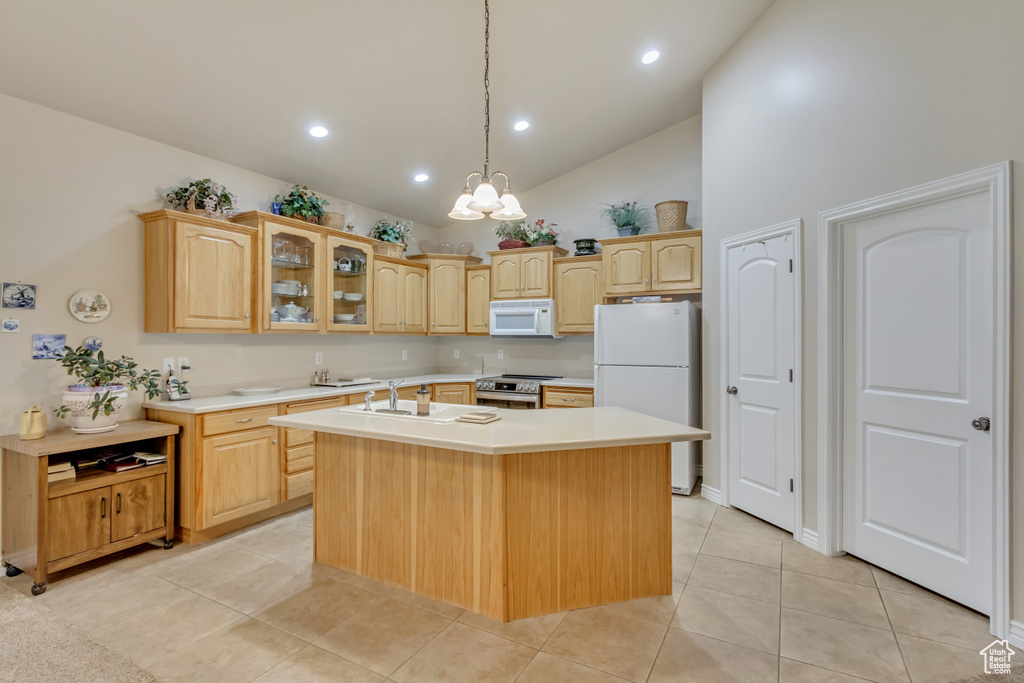 Kitchen with white appliances, light brown cabinets, light countertops, an island with sink, and high vaulted ceiling