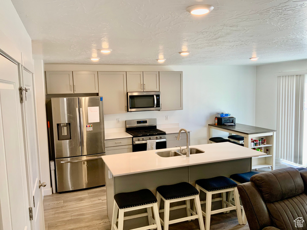 Kitchen featuring appliances with stainless steel finishes, gray cabinetry, light wood-type flooring, a kitchen bar, and light countertops