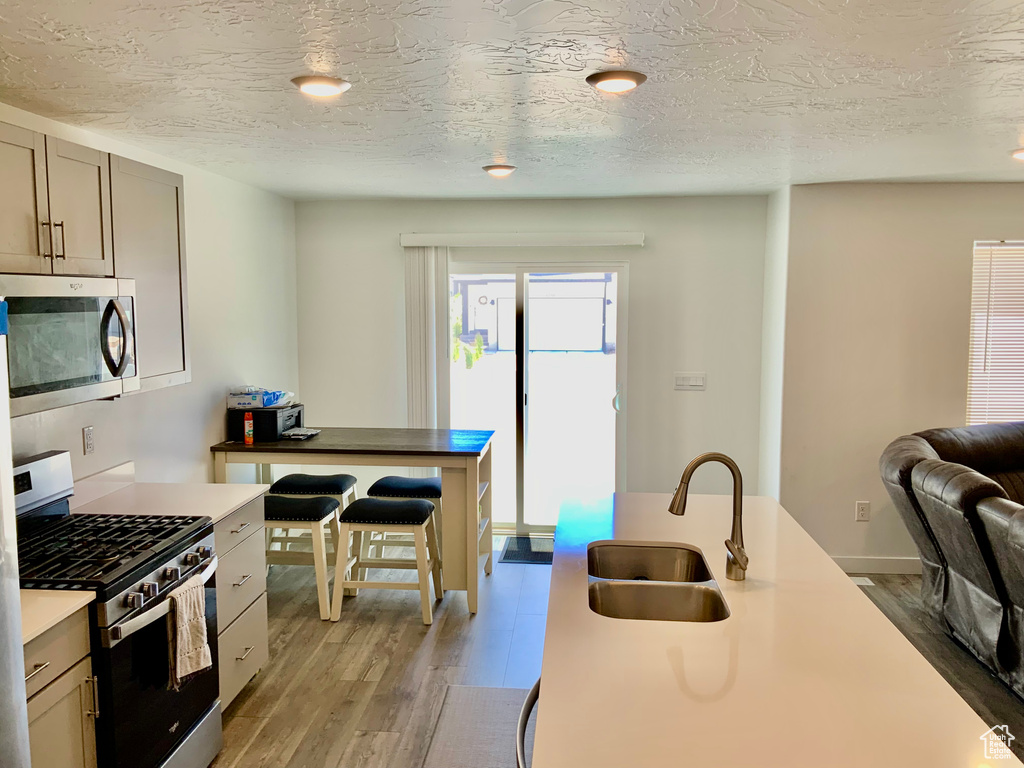 Kitchen with stainless steel appliances, light wood-type flooring, a textured ceiling, and open floor plan