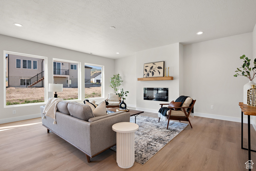 Living area featuring wood finished floors, recessed lighting, a glass covered fireplace, and a textured ceiling