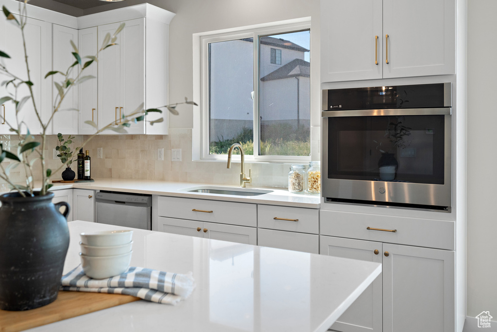 Kitchen with stainless steel appliances, white cabinets, tasteful backsplash, and light countertops