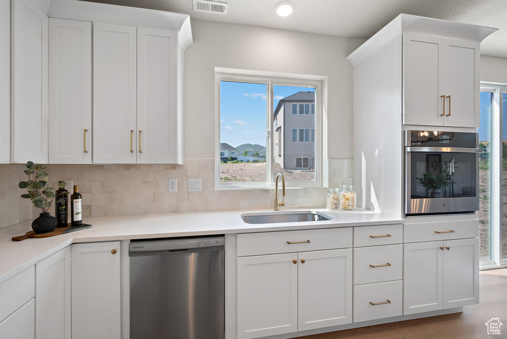 Kitchen with stainless steel appliances, white cabinetry, decorative backsplash, and light countertops
