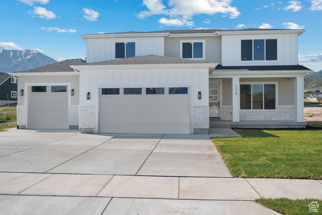 View of front facade featuring an attached garage, stone siding, driveway, and board and batten siding