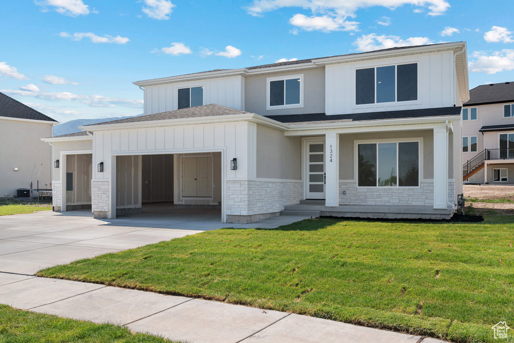 View of front of property featuring stone siding, concrete driveway, board and batten siding, a garage, and a front lawn