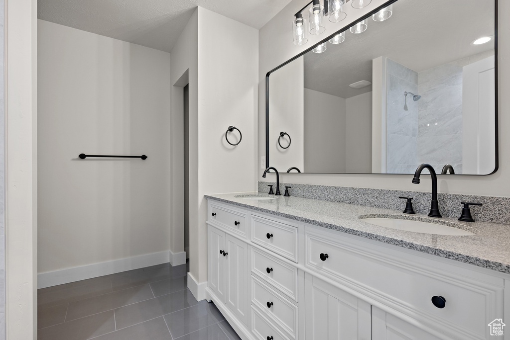 Bathroom featuring double vanity, tile patterned flooring, and a tile shower